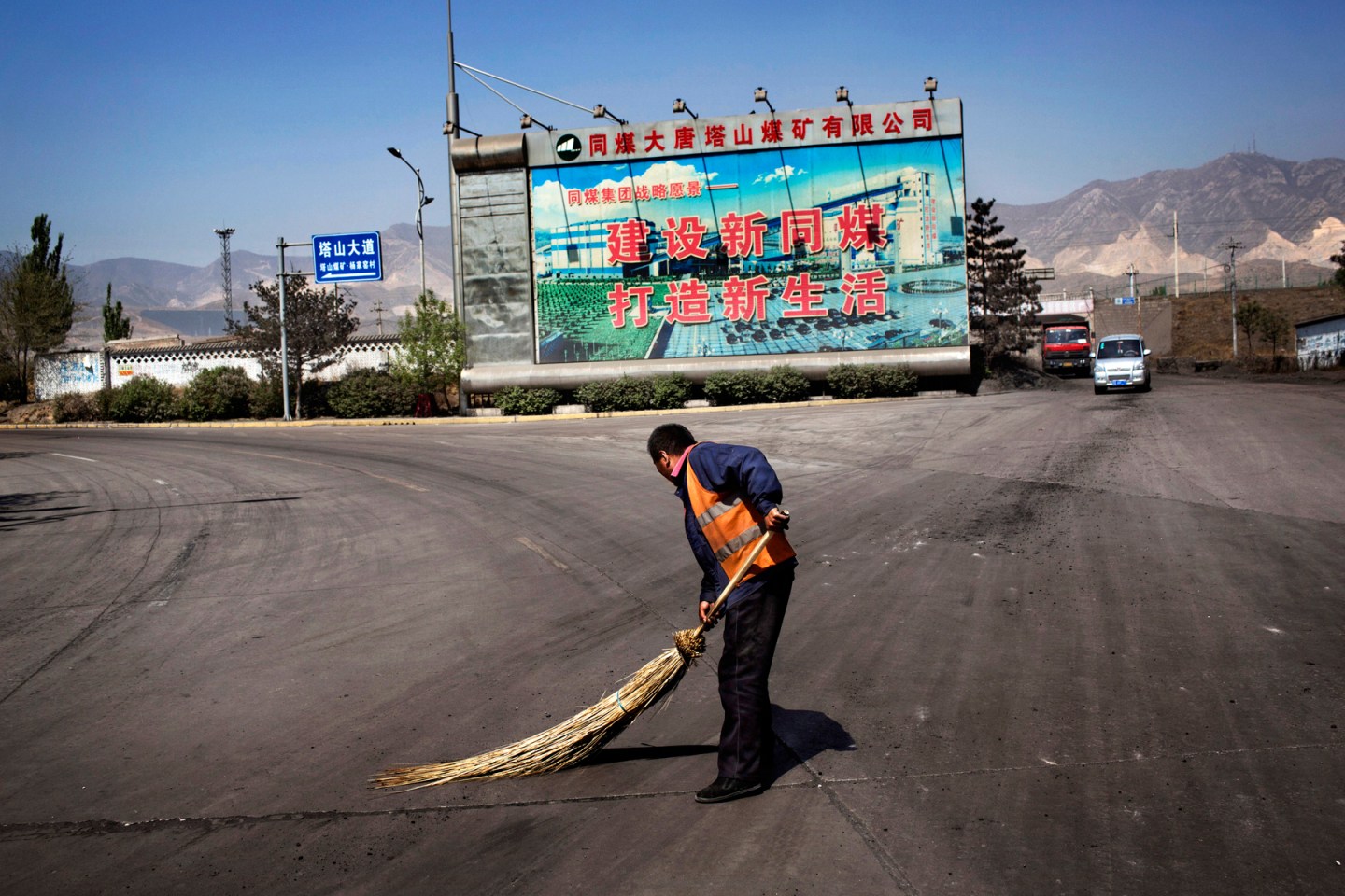 A worker sweeps coal dust in front of a billboard