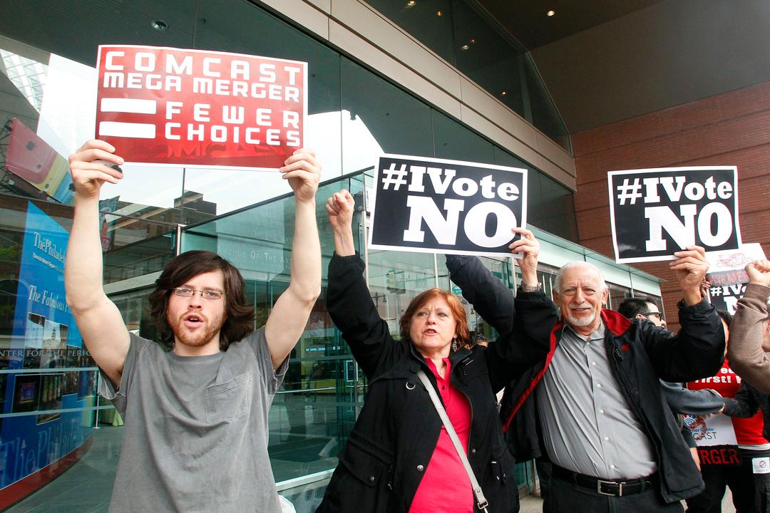 Three of a group of local residents and consumers organizations opposing Comcast's proposed merger with Time Warner Cable protest the deal outside the Comcast Shareholders Meeting in Philadelphia