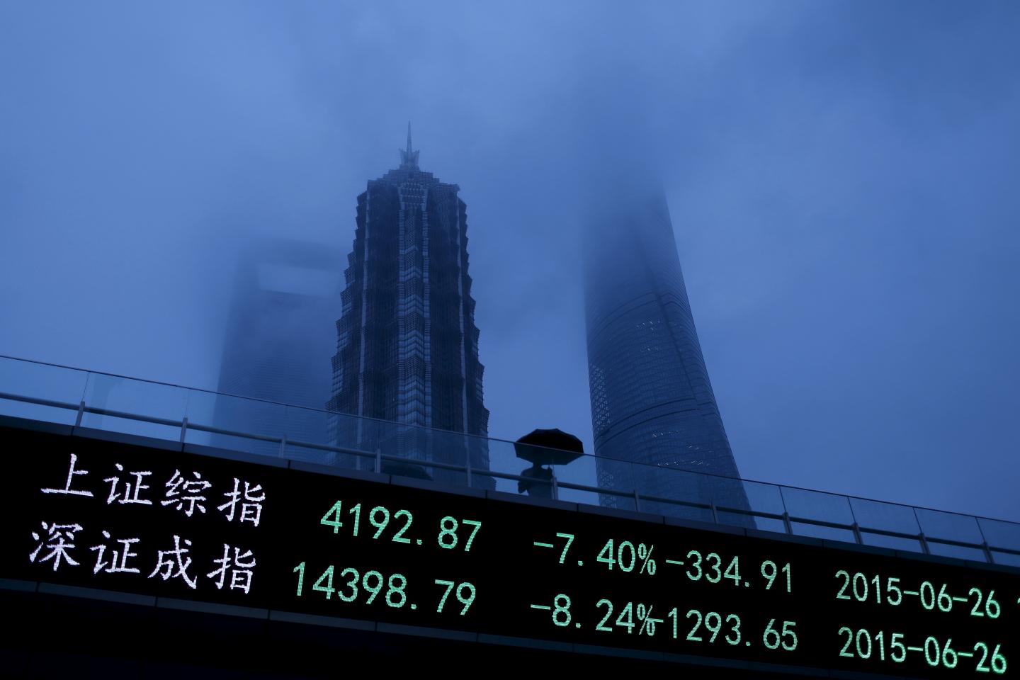 A man walks past an electronic board showing the benchmark Shanghai and Shenzhen stock indices, on a pedestrian overpass at the Pudong financial district in Shanghai