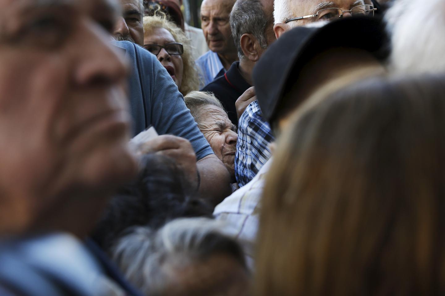 A pensioner is squeezed as she waits outside a National Bank branch to receive part of her pension in Athens
