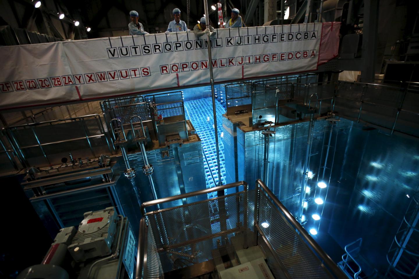 Employees of Kyushu Electric Power Co. hoist a fuel rod using a crane from a spent fuel pool at Sendai nuclear power station, in Satsumasendai