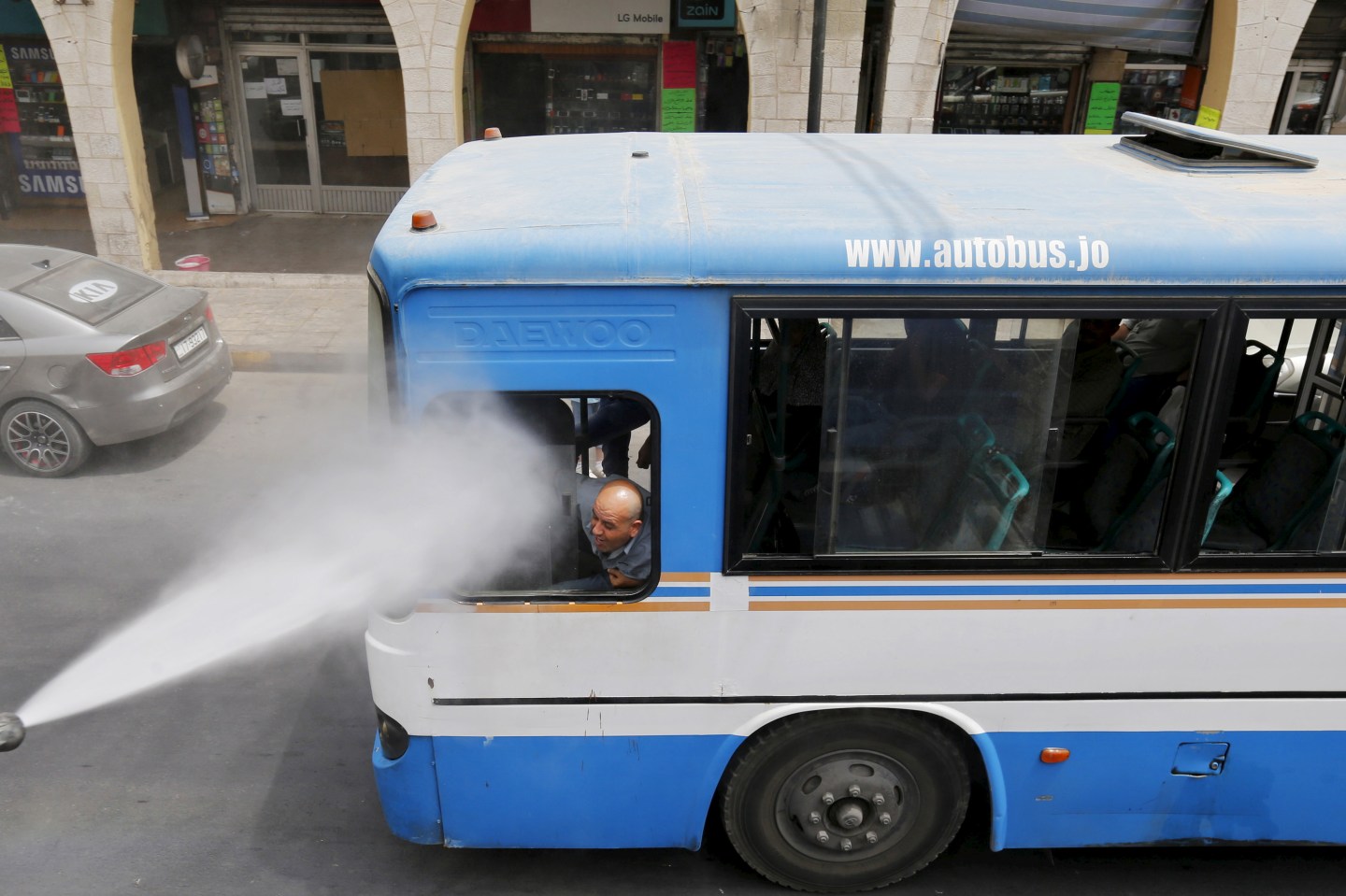 A bus driver reacts as Greater Amman Municipality personnel spray them with a water sprinkler in order to cool them down as part of measures to ease the effect of a heatwave, in Amman