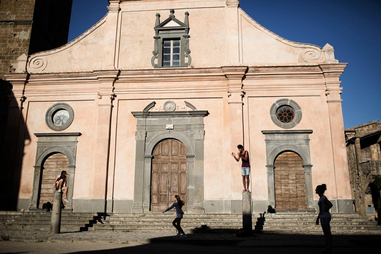 A family on vacation from Puglia plays on the columns outside the San Donato Church in Civita di Bagnoregio, Italy.