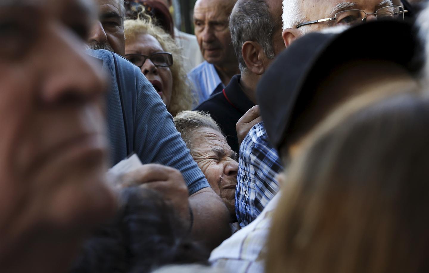 A pensioner is squeezed as she waits outside a National Bank branch to receive part of her pension in Athens