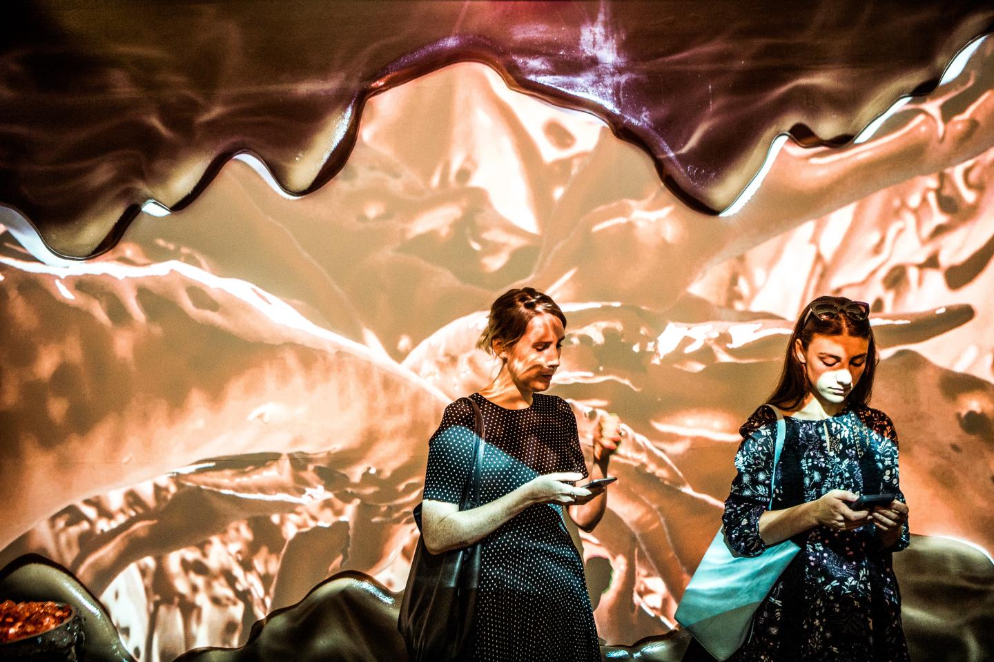 Attendees pass through the chocolate room, where projections of liquid chocolate swirl along the wall, during a press preview of the Museum of Ice Cream in New York.