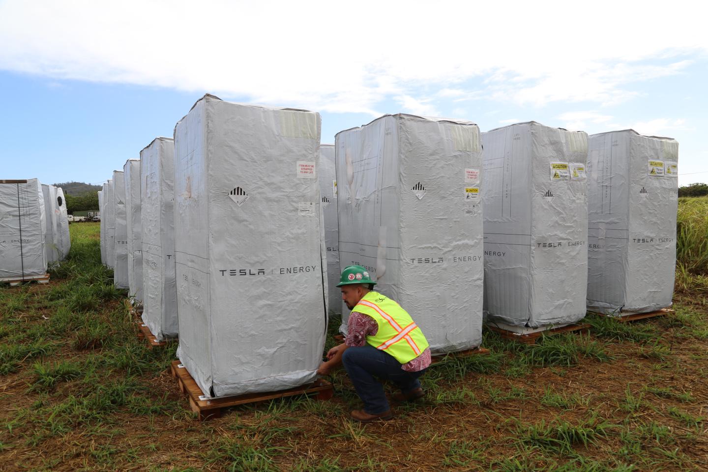 Tesla batteries await installation at a solar panel farm built by SolarCity for Kauai Island Utility Cooperative on the Hawaiian island of Kauai. SolarCity Senior Commercial Project Manager Danny Valdez unzips the battery's cover.