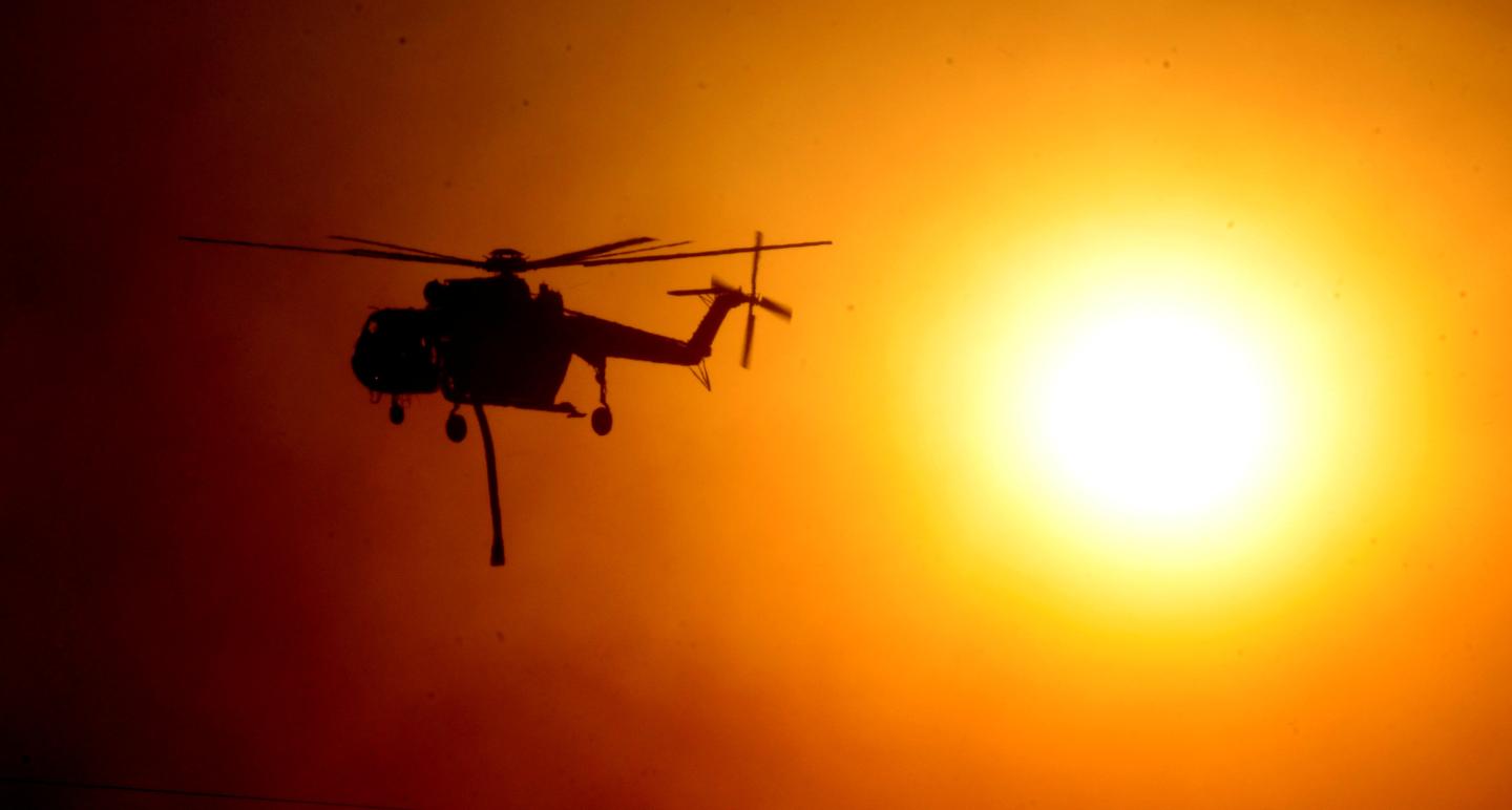 A firefighting helicopter passes by the smoke covered sun during an early-morning Creek Fire that broke out in the Kagel Canyon area in the San Fernando Valley north of Los Angeles in Sylmar