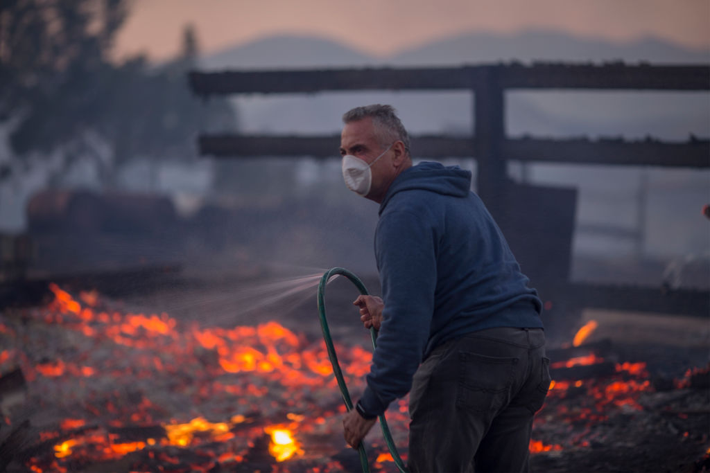 Man wearing face mask sprays fire with hose during California wildfire in December 2017.