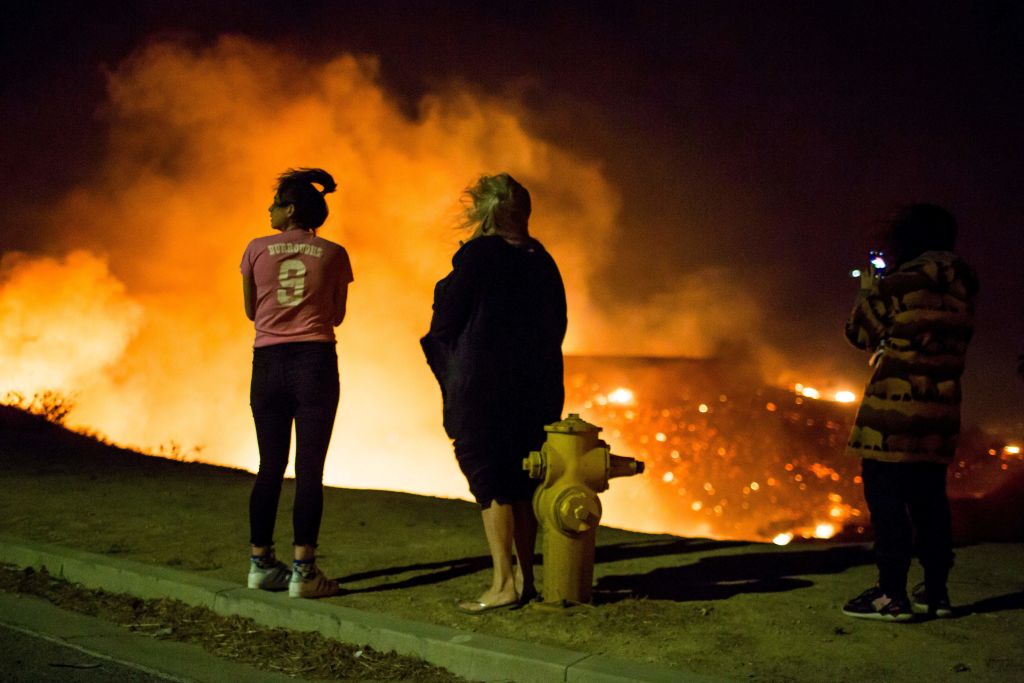 California residents stand near hydrant and watch wildfire engulf California hillside.