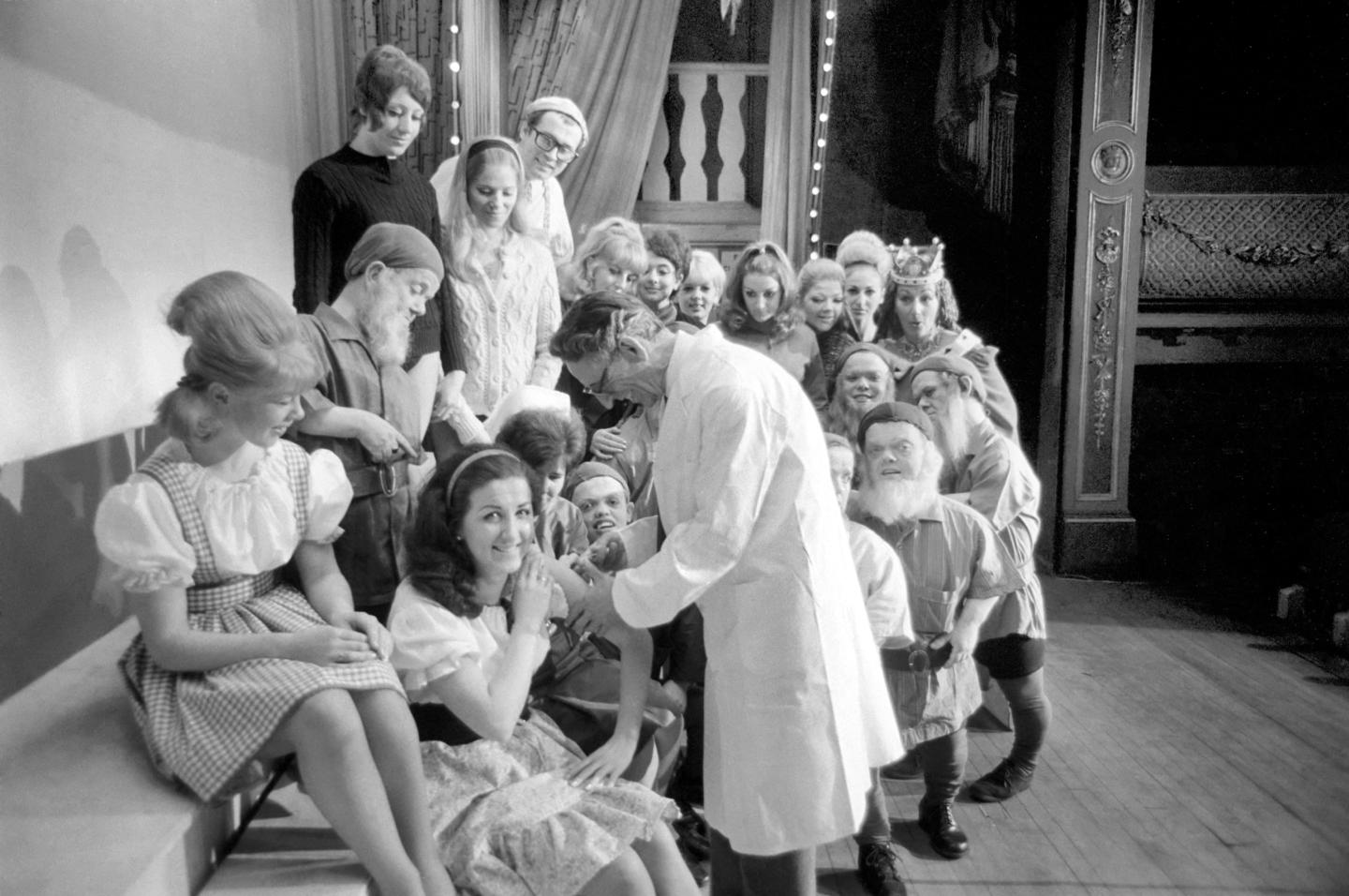 A doctor with his syringe makes ready to give anti-flu vaccine to Margaret Ayre, who plays Snow White and the rest of th