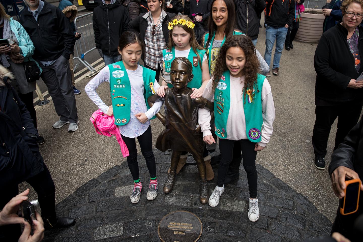 Three Girl Scouts in green vests pose with Fearless Girl statue