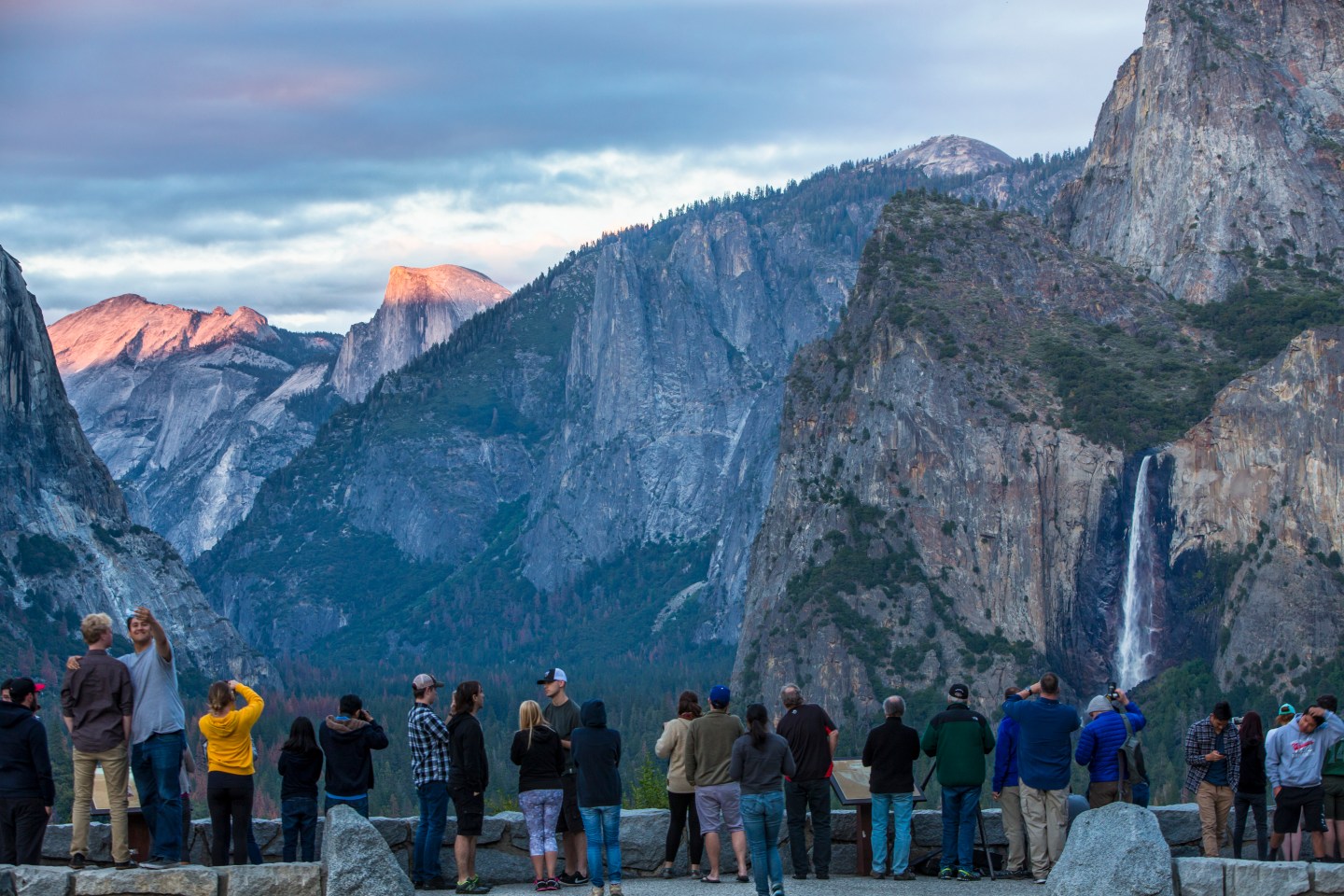 visitors take photos and enjoy the sunset overlooking the Yosemite Valley floor at sunset.