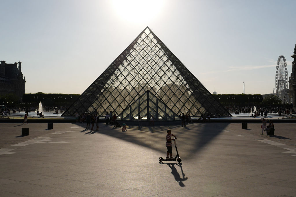 A boy rides an electric scooter in front of the Pyramid of The Louvre Museum in early July, 2019.