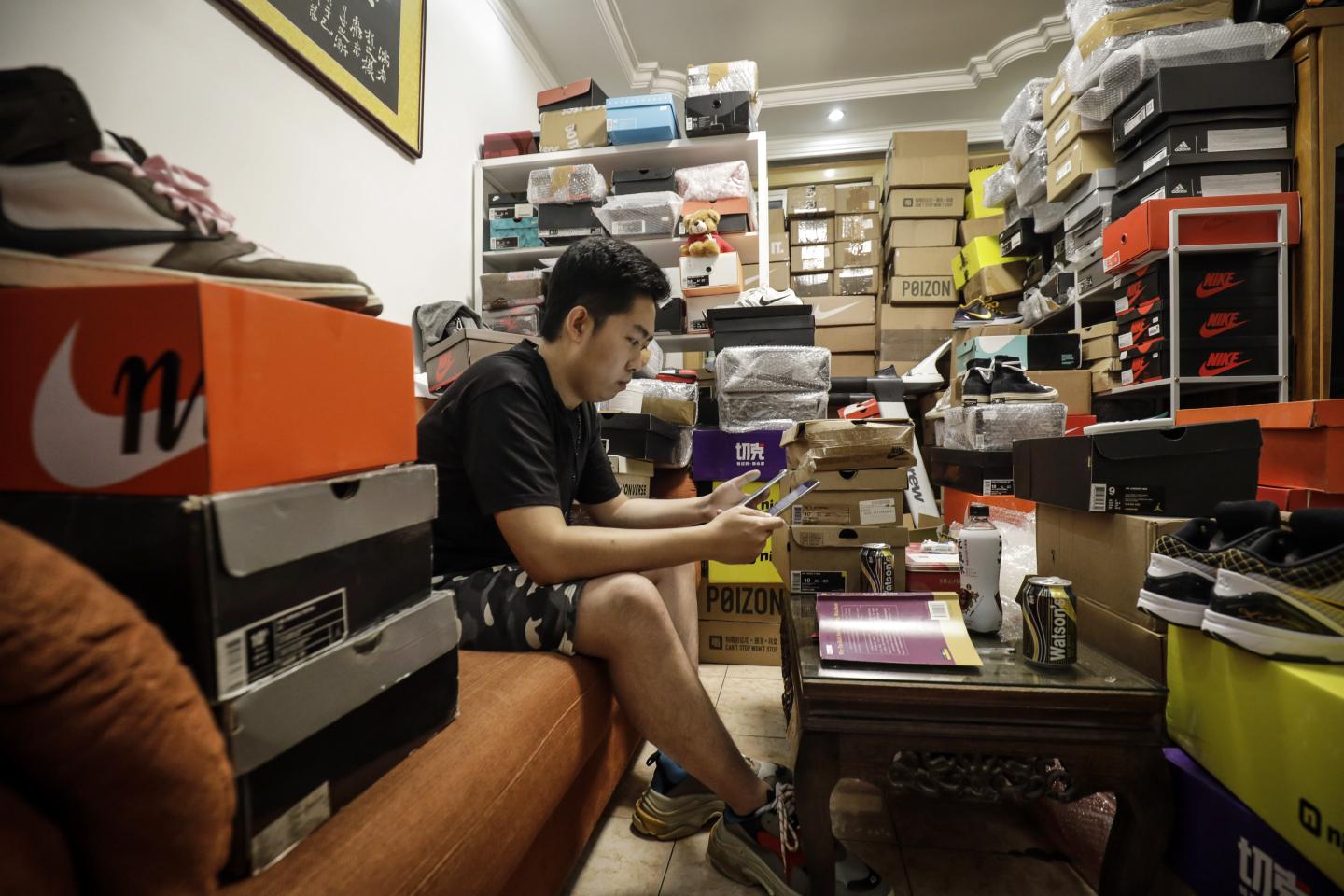EDITOR'S NOTE: ONE TIME USE ONLY IN CONNECTION WITH 'Chinas Sneakerheads Chase 6,600% Returns Flipping Air Jordans' by Bloomberg News. EDITORIAL USE ONLY. NO SALES. NO ARCHIVING. Tian Hao, a sneaker collector and trader, browses a trading app while sitting among boxes of sports shoes crammed into the living room of his home in Beijing, China, on Wednesday, Sept. 25, 2019. Across China, more than 10 million monthly active users frequent online-resale apps for sneakers, such as Poizon, Nice and DoNew, according to Chinese data-mining company QuestMobile. While many products suffer from the effects of the trade war, pairs of collectible sneakers are flying off the shelves, and that's attracting the attention of U.S. sneaker exchanges like StockX and GOAT. Photographer: Qilai Shen/Bloomberg via Getty Images