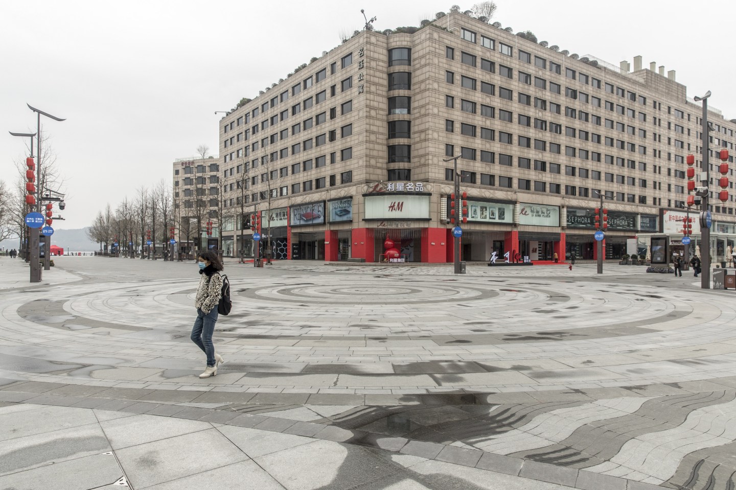 A pedestrian wearing a face mask walks through an empty shopping plaza, in view of a H&M store, in Hangzhou, China, on Feb. 11, 2020.