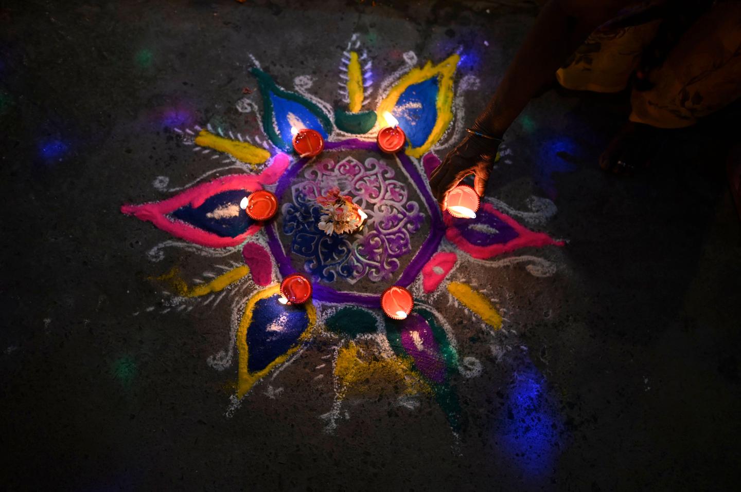 A woman places an oil lamp or "diya" on a rangoli during celebrations for the Hindu festival Diwali or the Festival of Lights in New Delhi on November 4, 2021.
