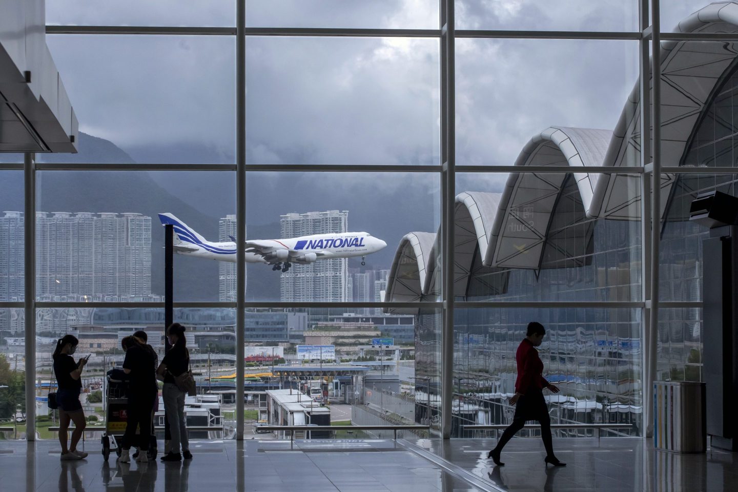 A photo of travelers as a National Airlines cargo plane lands behind them at the Hong Kong International Airport in August, 2021.