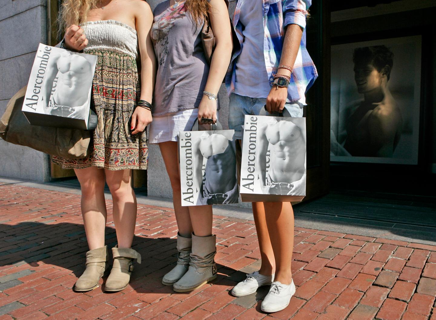 Three girls hold Abercrombie and Fitch shopping bags with shirtless men on them