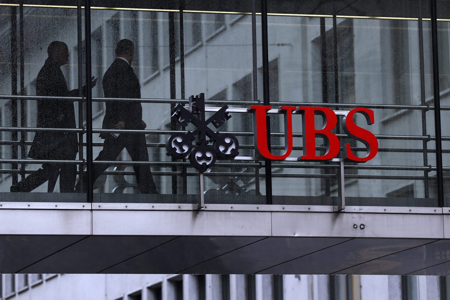 Employees pass between offices as UBS Group AG logo sits on a walkway at the UBS headquarters in Zurich, Switzerland