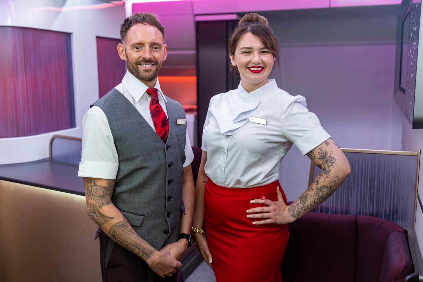 Two uniformed Virgin Atlantic cabin crew members are pictured with their arm tattoos on display.