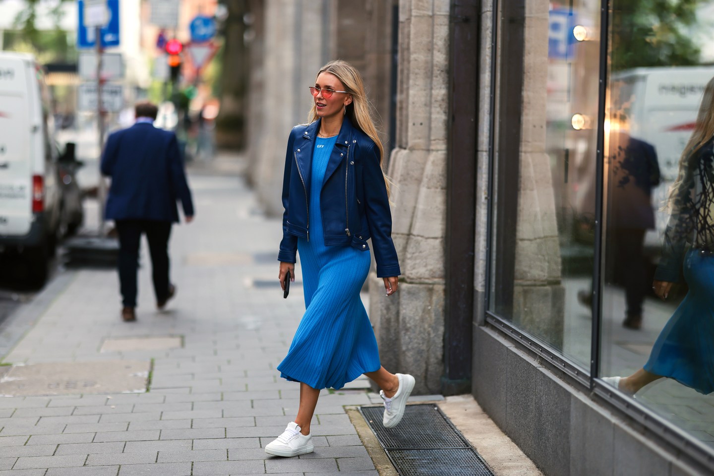 Woman wearing blue flowy summer dress and white sneakers walks out of building.
