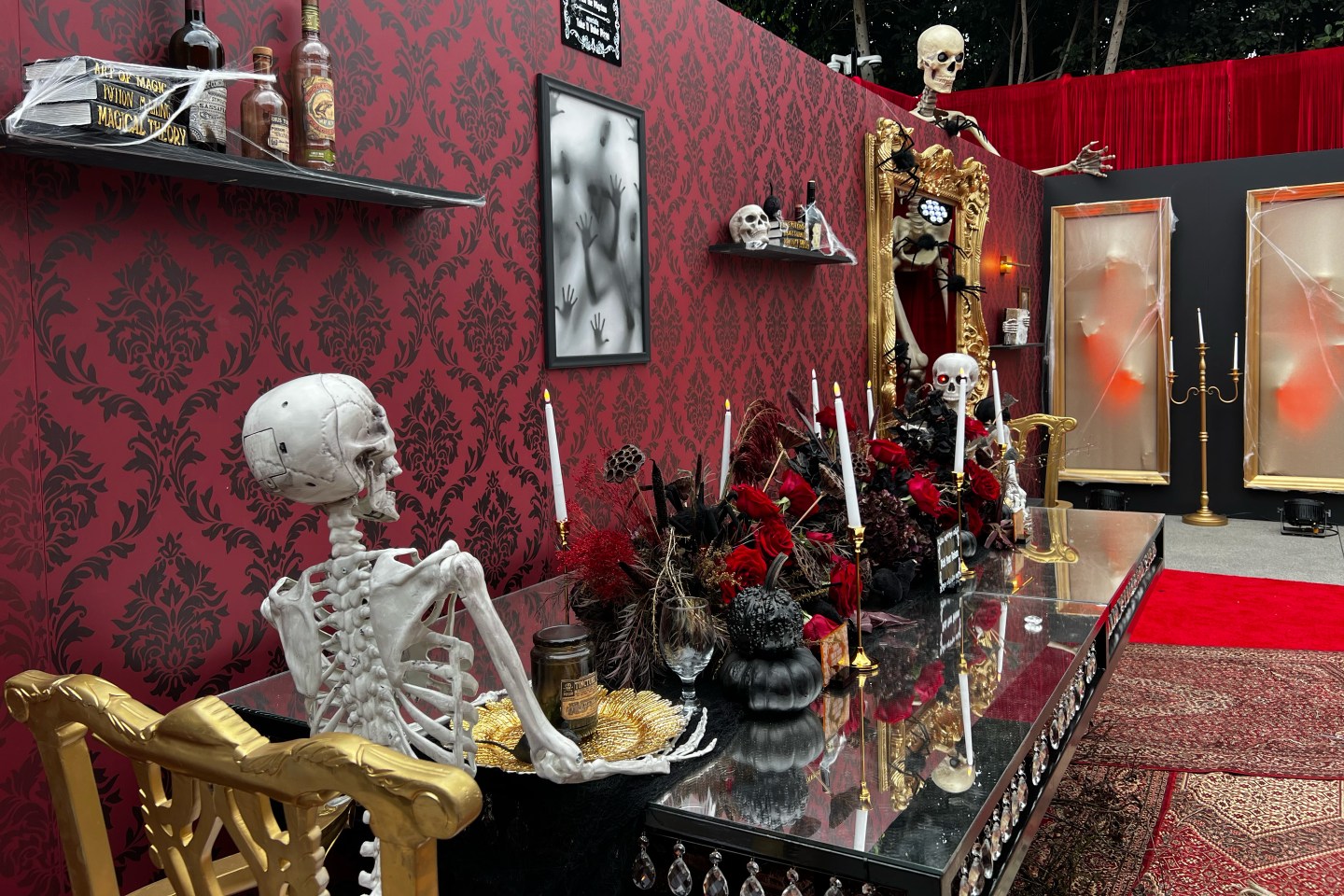 Fake skeletons sitting at a table laden with black pumpkins.