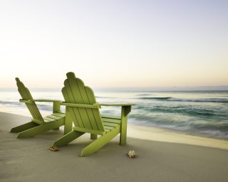 Two beach chairs on the beach facing a still horizon. Horizontal shot.