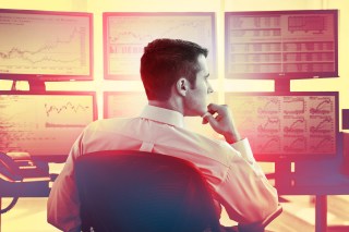 Male trader at work in front of computer monitors with stock market data