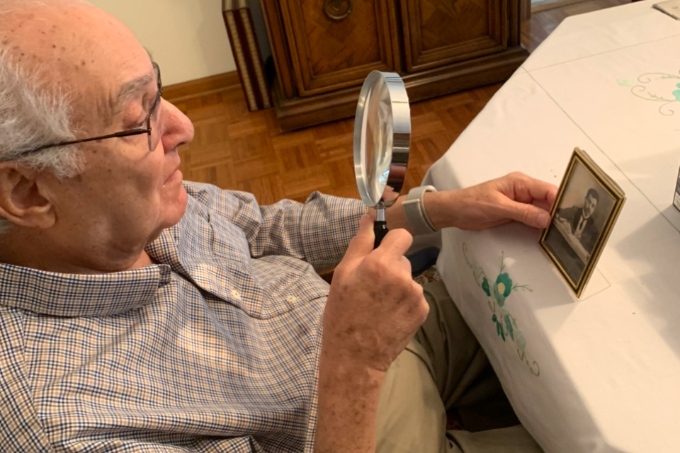 An elderly man using a magnifying glass to view old photos