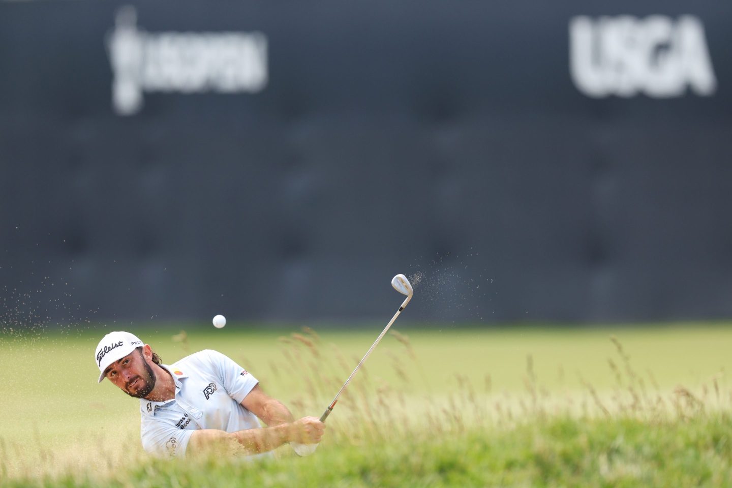 Max Homa hits a golf ball out of a sand trap.