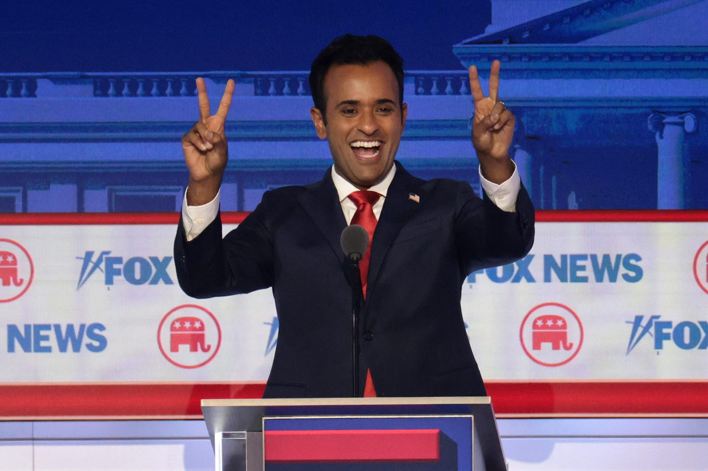 Republican presidential candidate Vivek Ramaswamy standing behind a podium holding up peace signs.