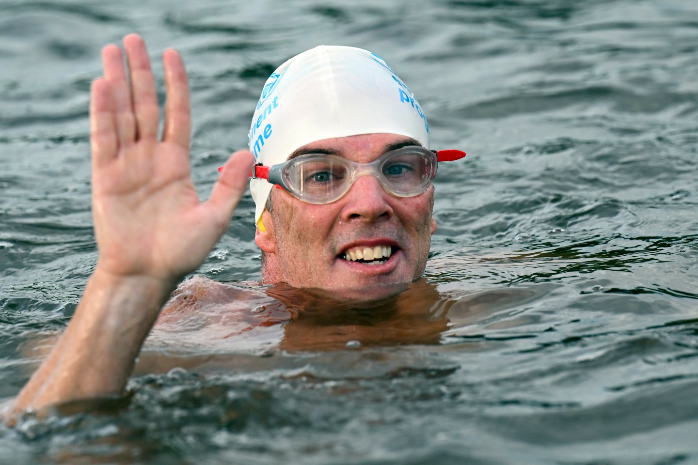 Pugh, wearing swimming cap and goggles, waves from the water.