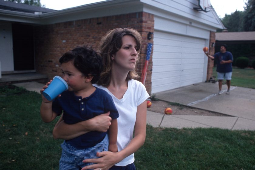 A woman holds a baby outside her home