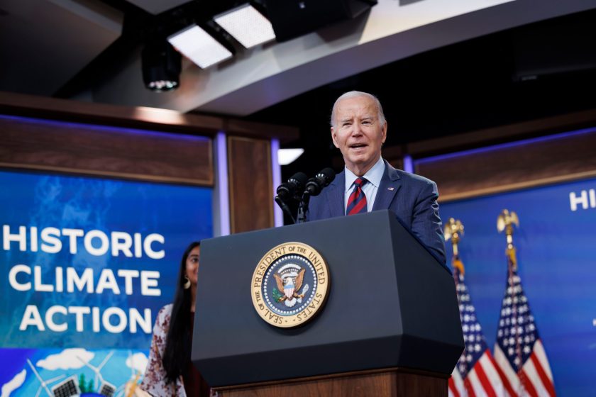 President Joe Biden stands in front of the presidential podium. In the background, the words 