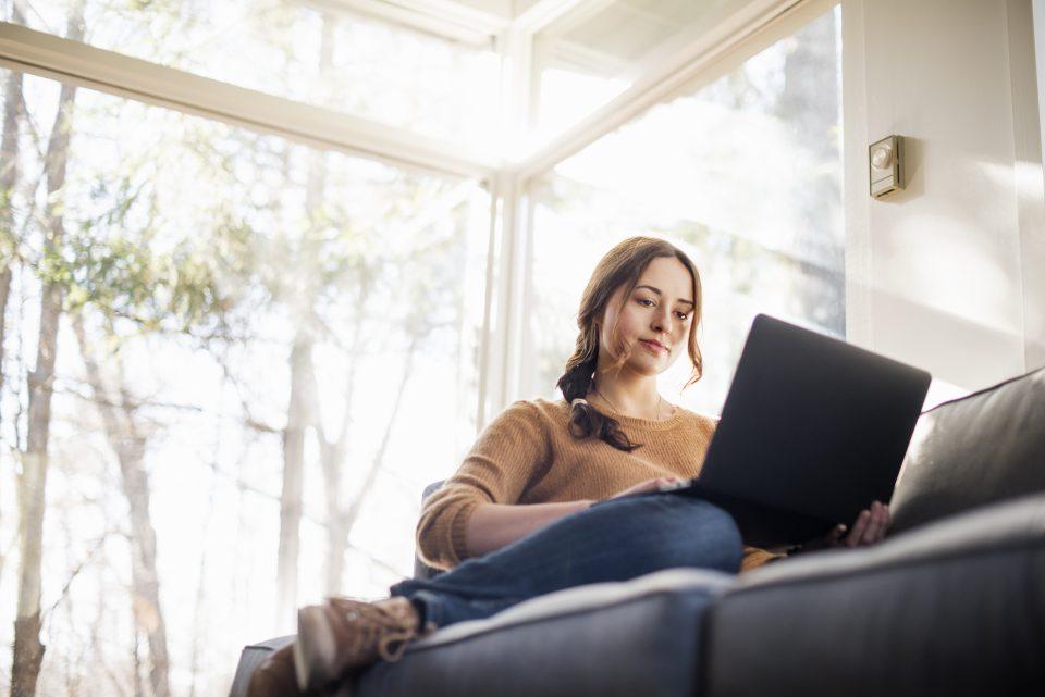 Low angle view of a woman sitting on a sofa looking at her laptop.